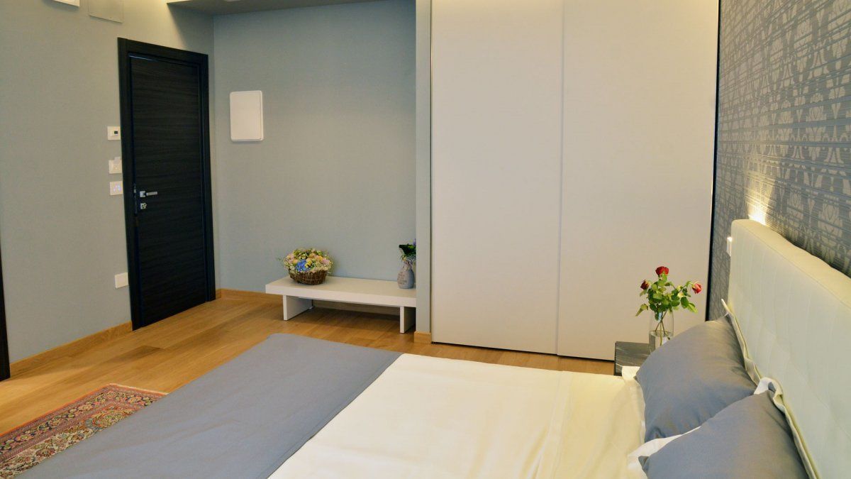 Un dormitorio con cama, un banco, una mesita con un florero y una puerta.