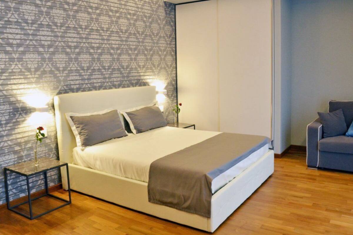 A bedroom with a bed, a chair, a nightstand, and a patterned wall.