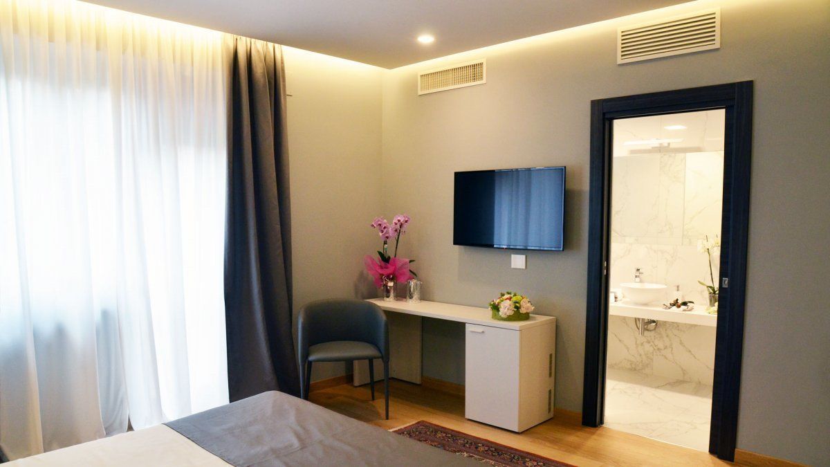 A hotel room with a bed, a desk, a chair, a TV, a bathroom with a sink and mirror, and a window with curtains.