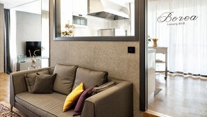 A modern living room with a sofa, a flat-screen TV, and a kitchen visible through a glass partition. - Borea Luxury B&B (Pescara)