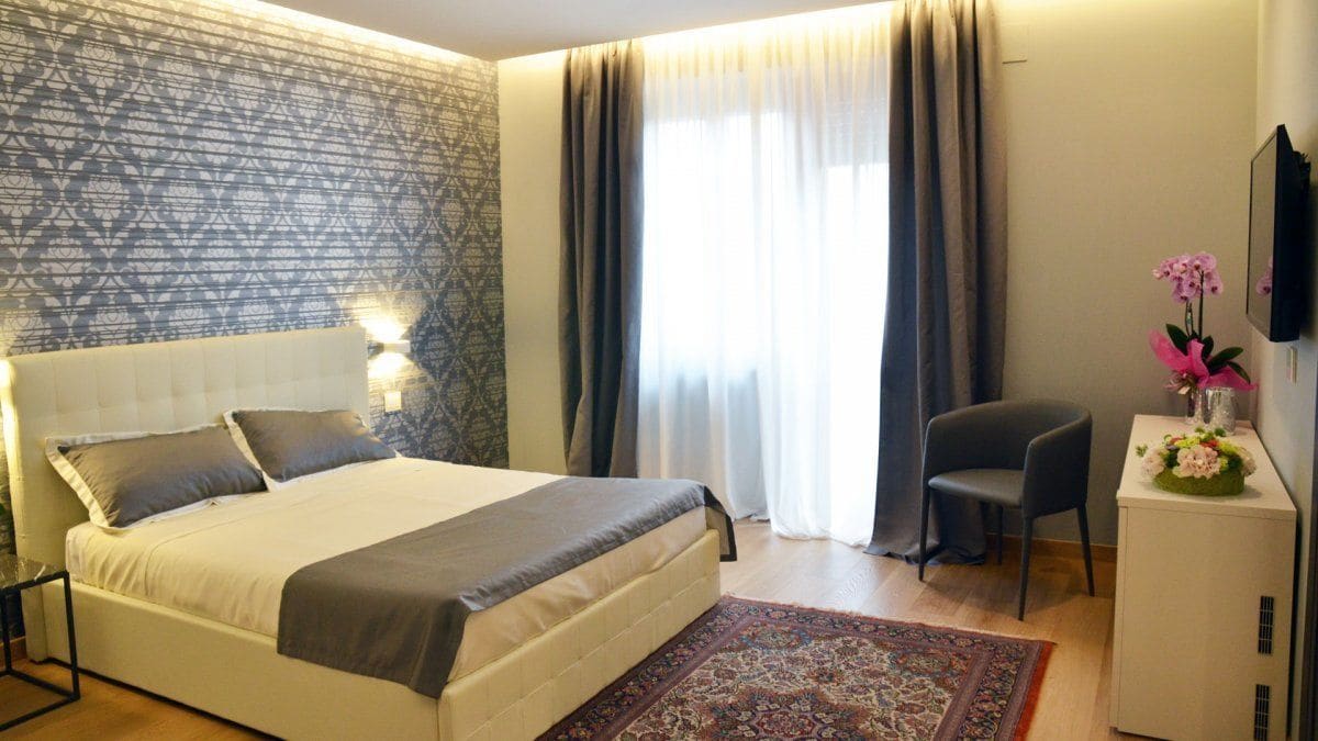 A modern hotel room with a large bed, a desk, a chair, and a TV.