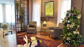 A living room with two armchairs, a coffee table, a large floral arrangement, and a painting on the wall. - Borea Luxury B&B (Pescara)