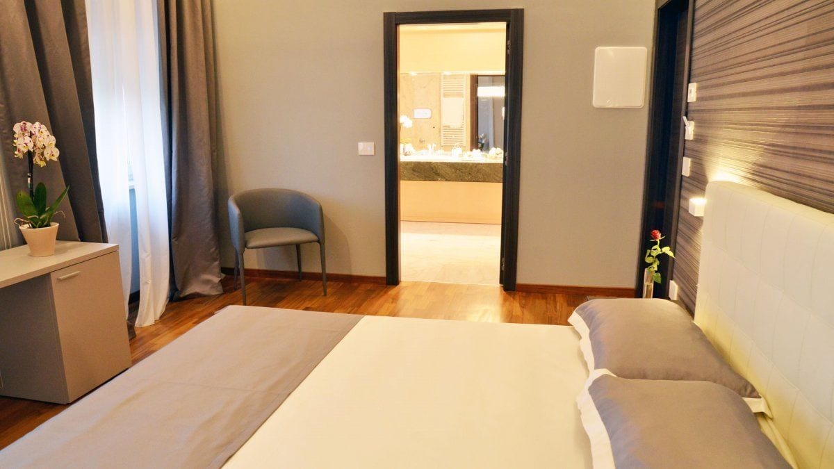 Habitación de hotel con cama, escritorio, silla y baño visible a través de una puerta abierta.