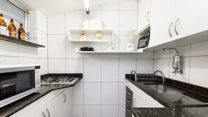 Una cocina moderna con armarios blancos, encimera negra, microondas integrado, estufa a gas, pileta con grifo y estanterías con utensilios de cocina.