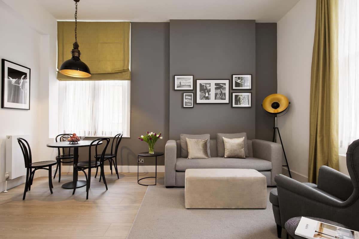 Una sala de estar moderna con un sofá gris, una mesa de comedor con sillas, una lámpara de pie y cuadros enmarcados en la pared.