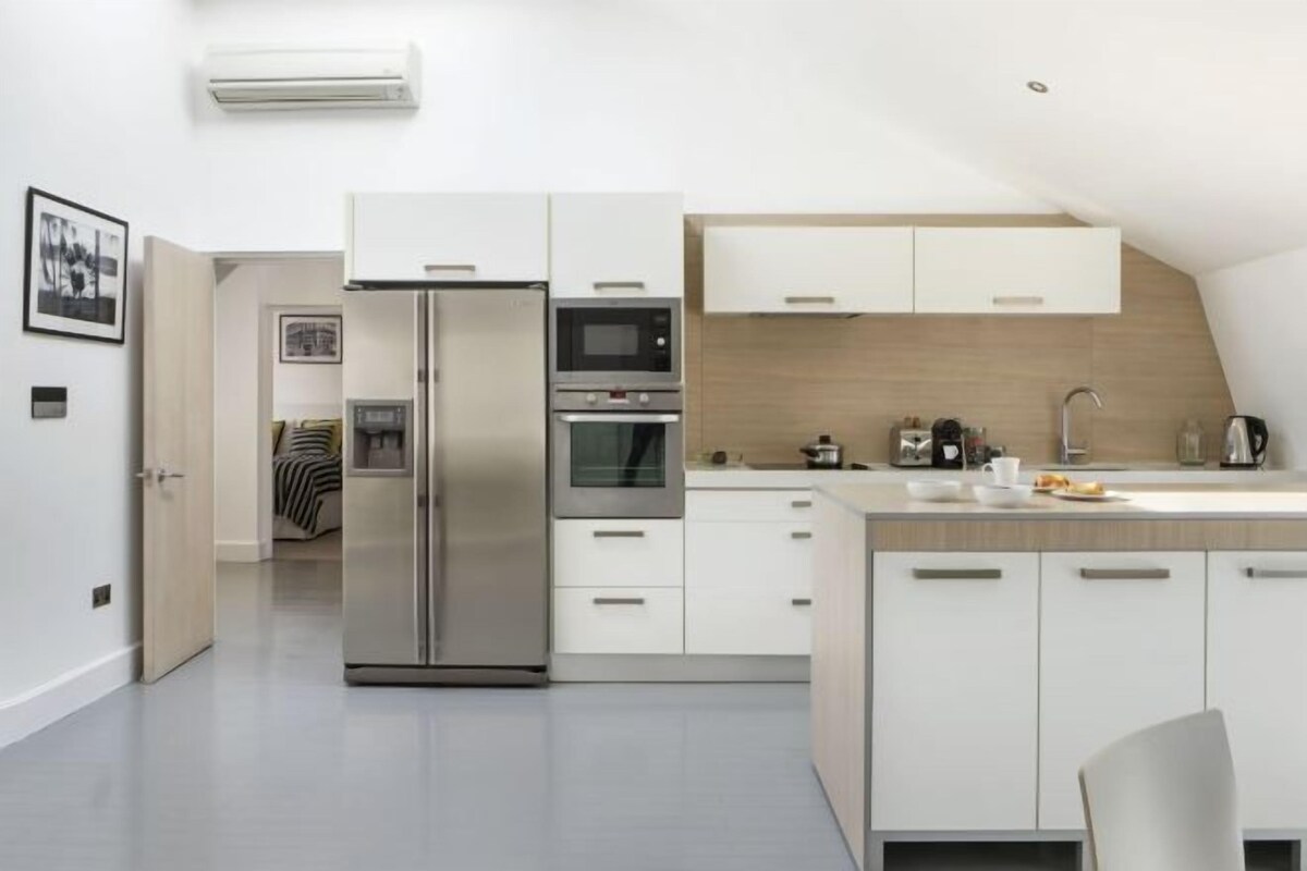 Una cocina moderna con una isla central, horno empotrado, microondas y refrigerador de acero inoxidable.