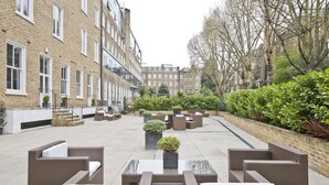 A courtyard with outdoor seating, brick buildings, and greenery. - Nevern Place by Supercity Aparthotels (London)