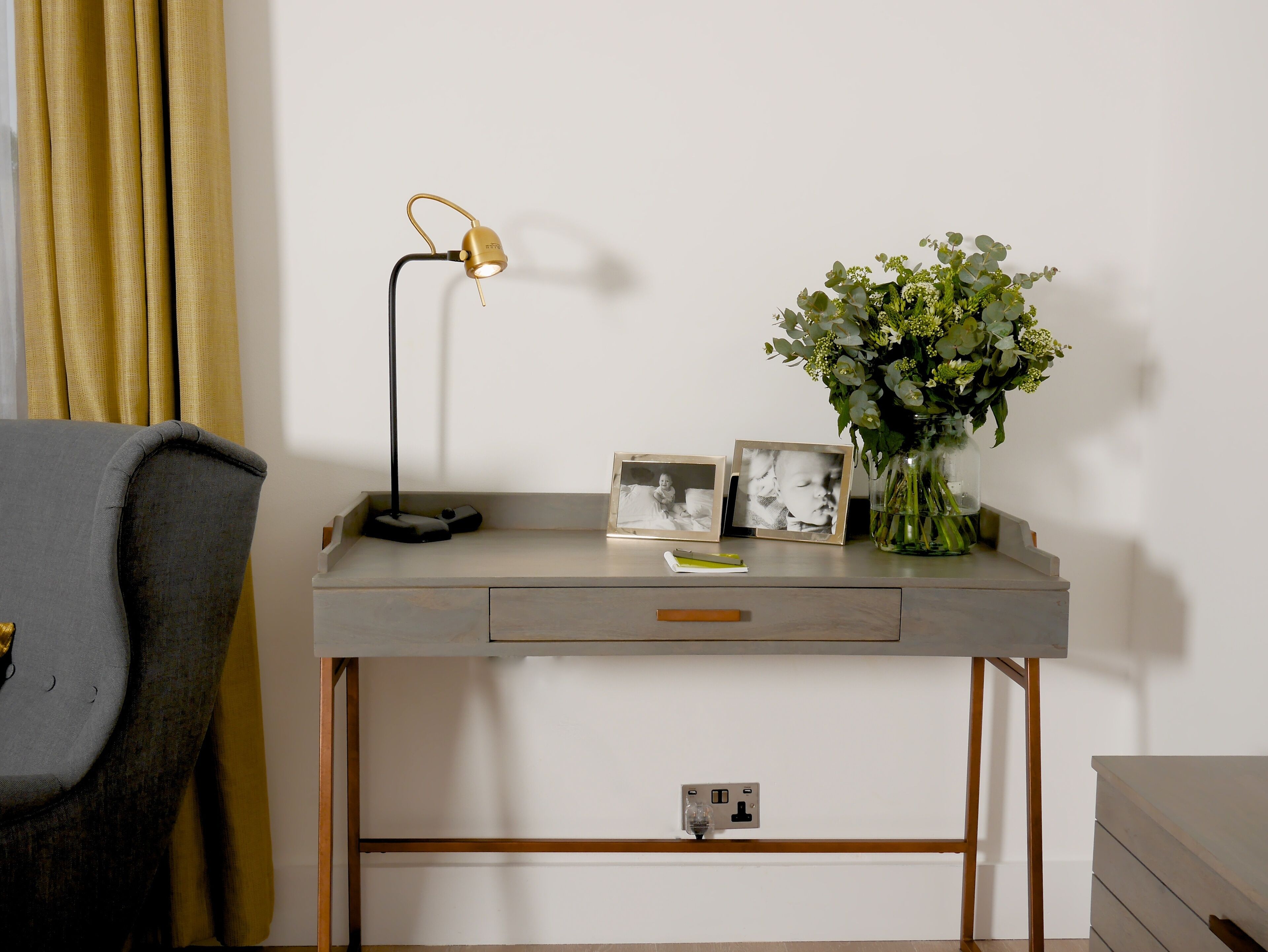 Una scrivania moderna con una lampada, cornici con fotografie e un vaso di fiori.