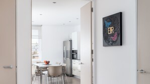 A modern kitchen with white cabinets and stainless steel appliances, a dining area with a table and chairs, and a hallway leading to a bedroom. - Nevern Place by Supercity Aparthotels (London)