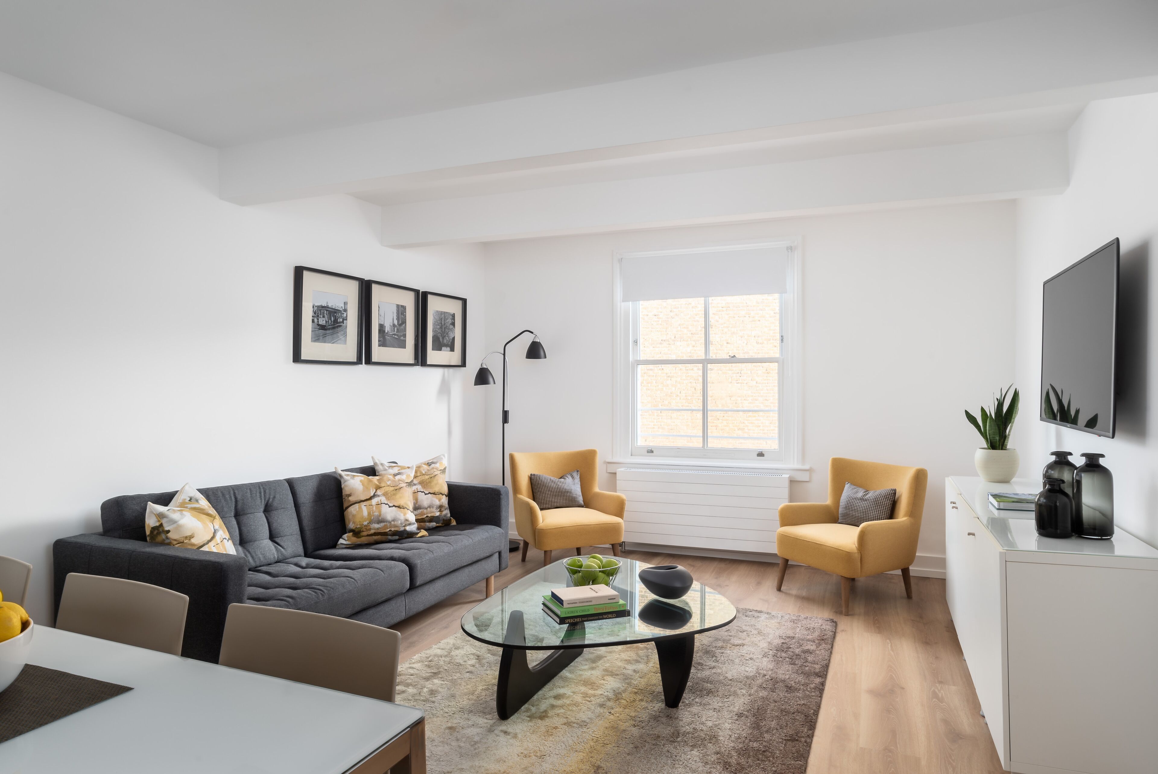 A modern living room with a sofa, armchairs, a glass coffee table, and a TV.