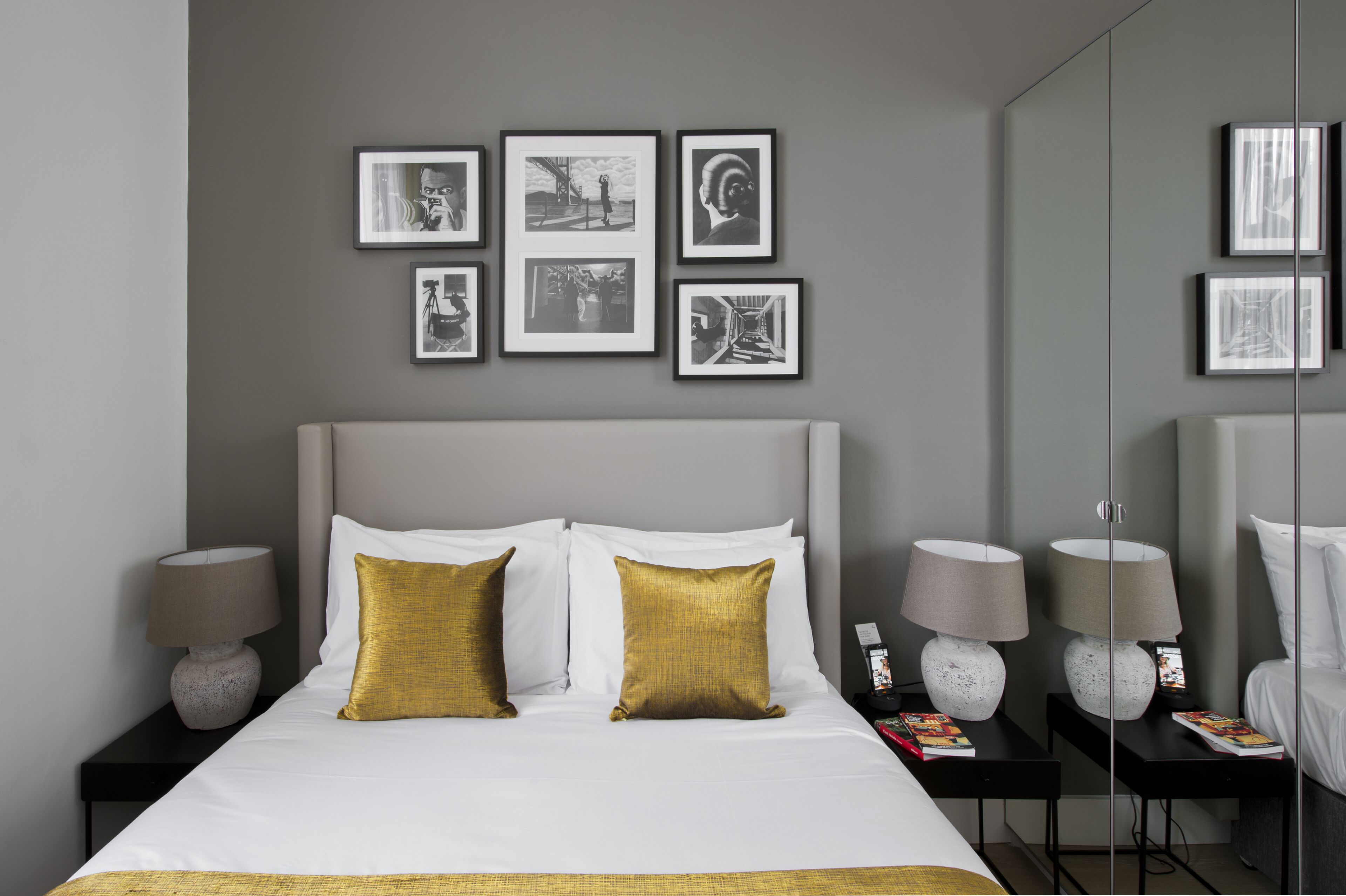 A neatly arranged hotel room with a large bed, two bedside tables with lamps, a wall-mounted mirror, and a series of framed pictures.