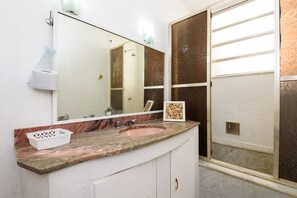Un baño con encimera de mármol, lavabo, espejo y cabina de ducha.