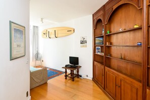 Una habitación con un armario de madera, una tabla de surf, un televisor sobre una mesita y un cuadro en la pared.