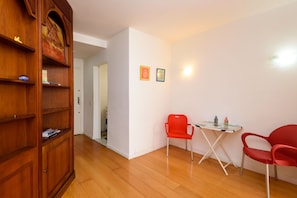 Una habitación con un armario de madera, una mesa de vidrio con dos sillas rojas y dos cuadros en la pared.