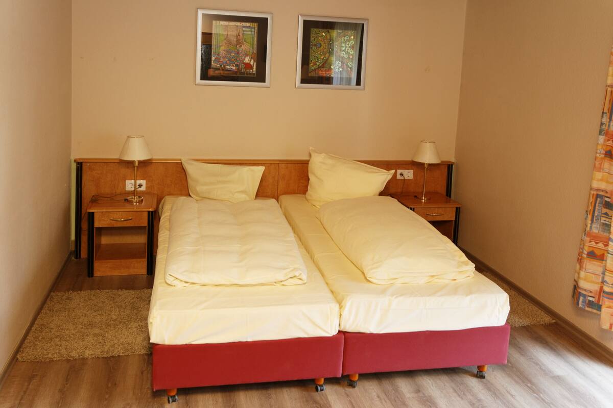 Un lit double avec une base rouge et une literie blanche, deux tables de chevet avec des lampes, et deux tableaux encadrés accrochés au mur.