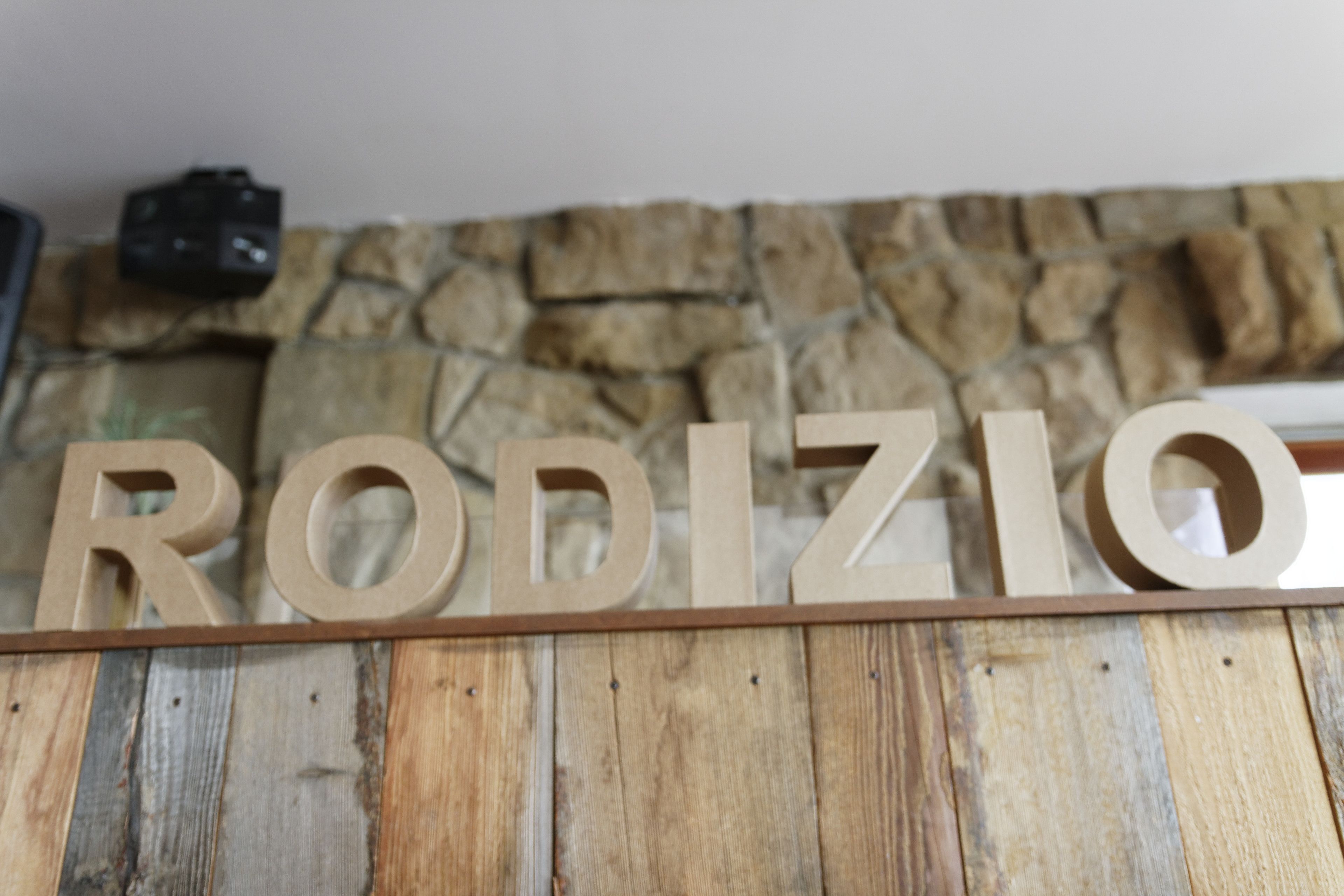 Een houten bord met de naam 'RODIZIO' bevestigd aan een stenen muur.