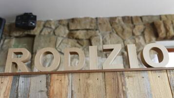 Een houten bord met de naam 'RODIZIO' bevestigd aan een stenen muur.