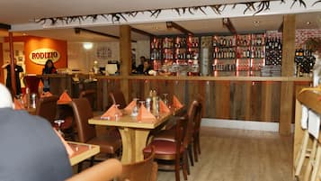 A restaurant interior with wooden tables and chairs, a bar area with shelves of bottles, and a sign for 'RODIZIO'.