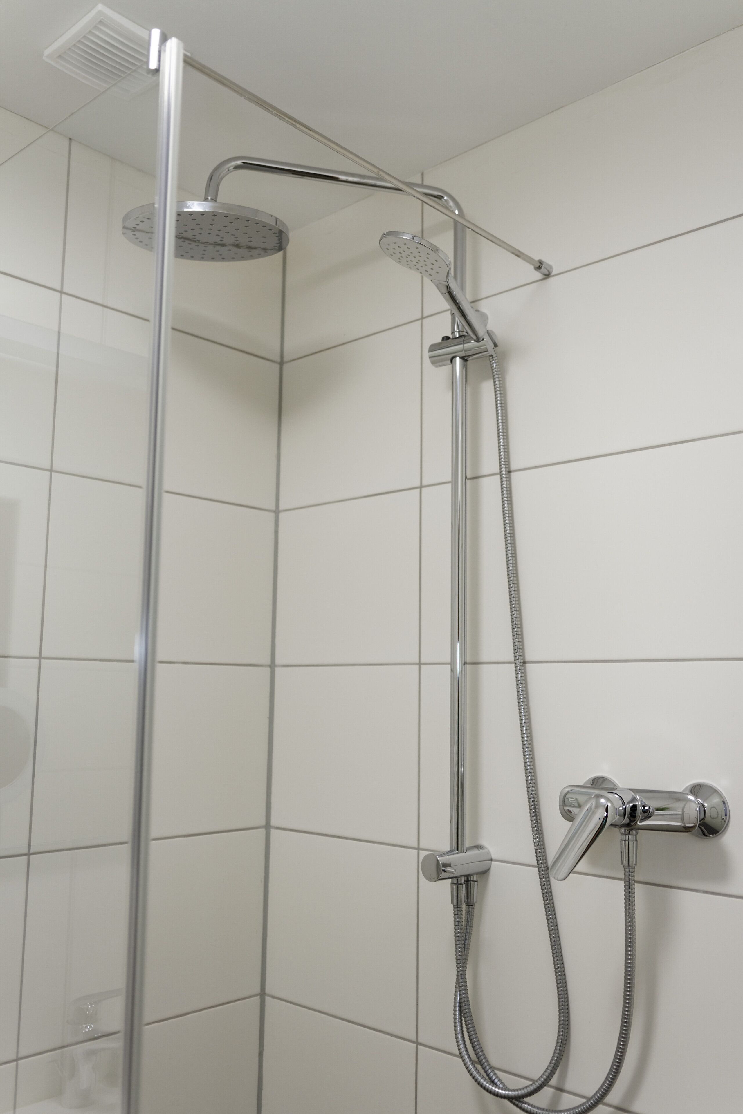 Ducha con cabezal de ducha de mano y otro fijo en la pared, ambos con acabados cromados.