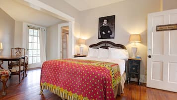 A bedroom with a large bed, two bedside tables with lamps, a chair, a door labeled "Bowie Suite," and a framed picture on the wall.