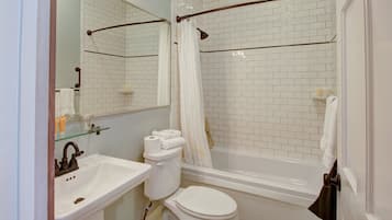 A bathroom with a white sink, toilet, and bathtub. There is a glass shelf above the sink and a towel rack next to the toilet.