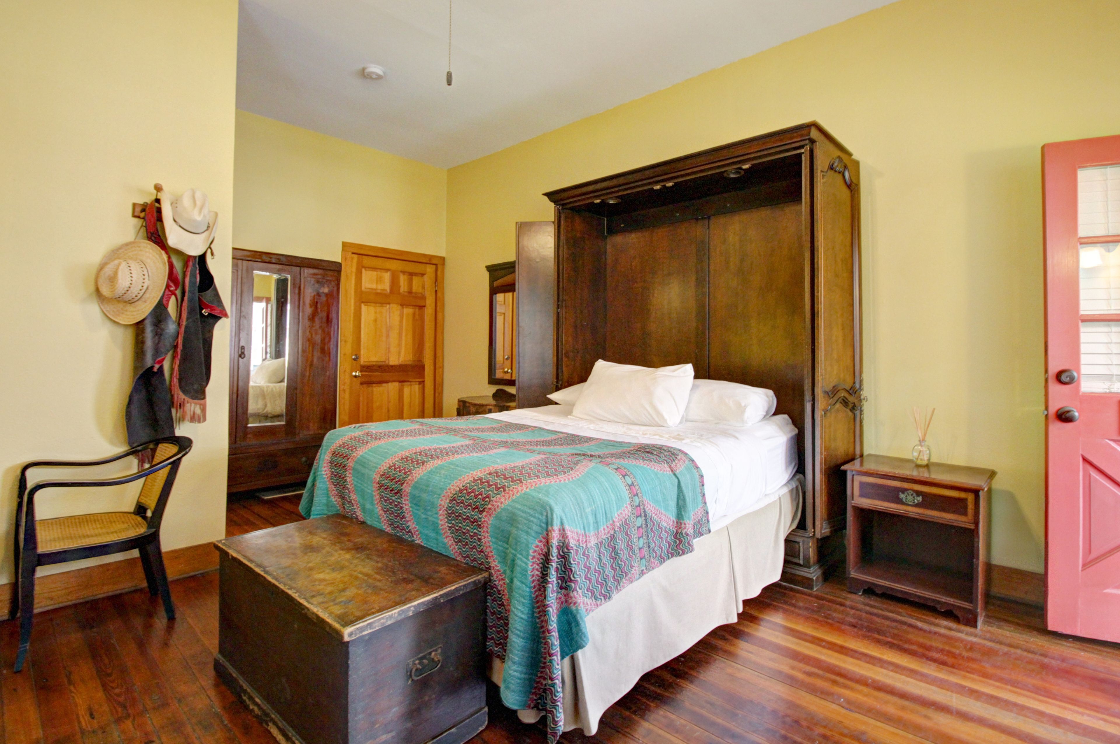 A room with a bed, a chair, a wooden cabinet, and a door.