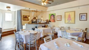 A restaurant with multiple tables and chairs, a ceiling fan, and artwork on the walls. - Inn on the Riverwalk (San Antonio)