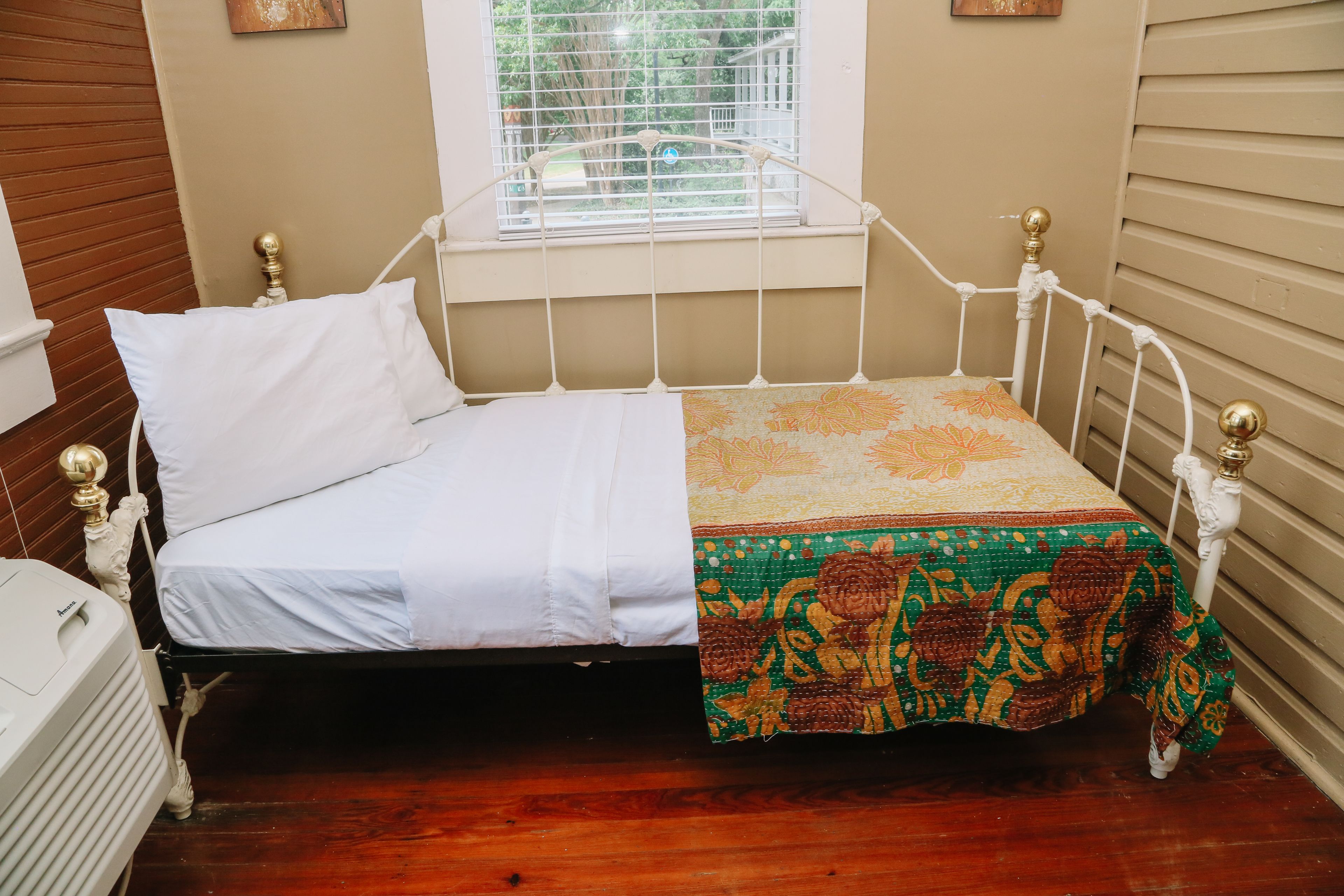 Un letto singolo con materasso bianco e trapunta colorata, una finestra vista verde e un termosifone a pavimento.