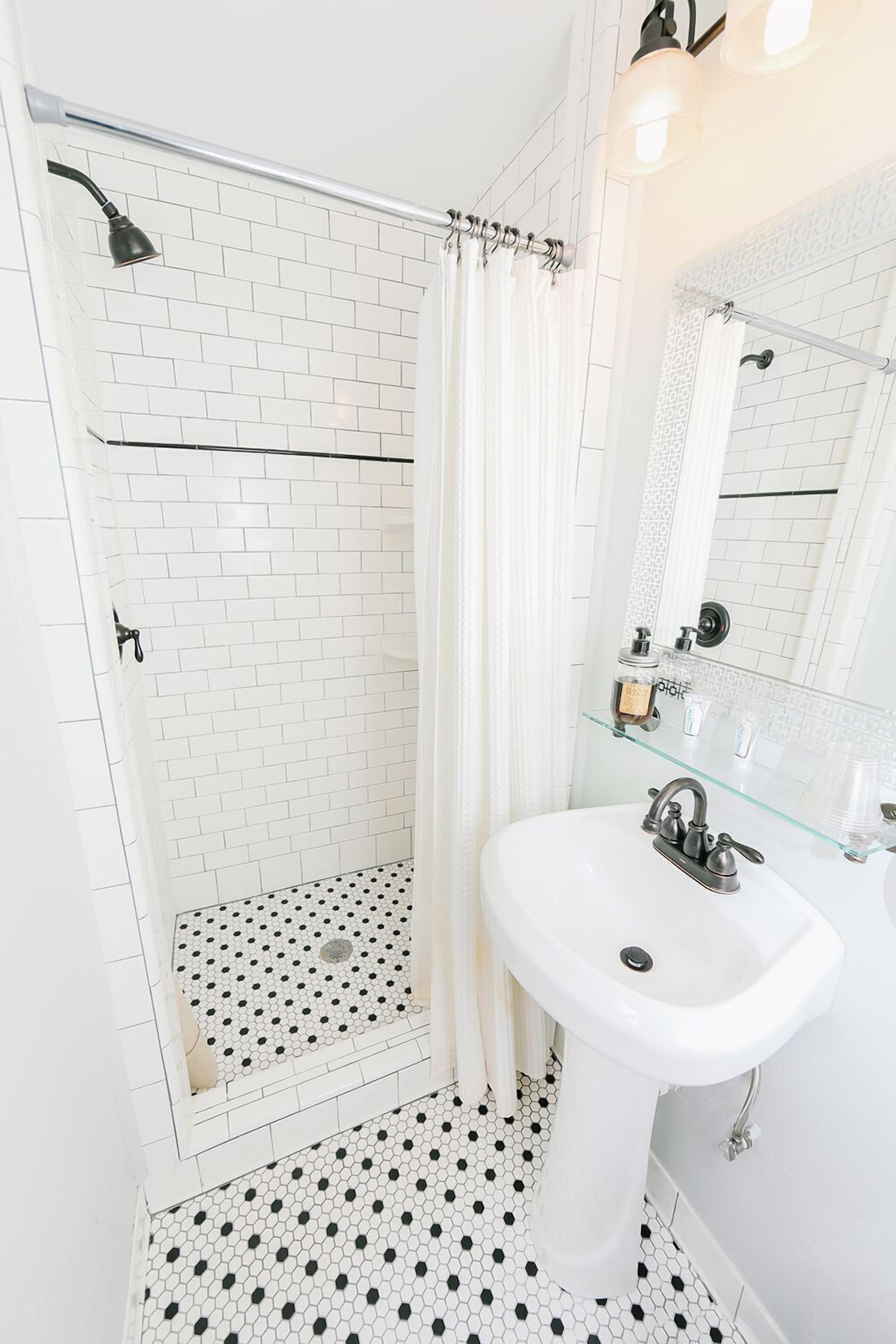 A bathroom with a glass shower enclosure, white tiled walls, a white sink, and a mirror.