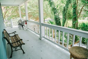 A covered porch with a wooden bench and a wicker chair, white railings, and a view of greenery. - Inn on the Riverwalk (San Antonio)
