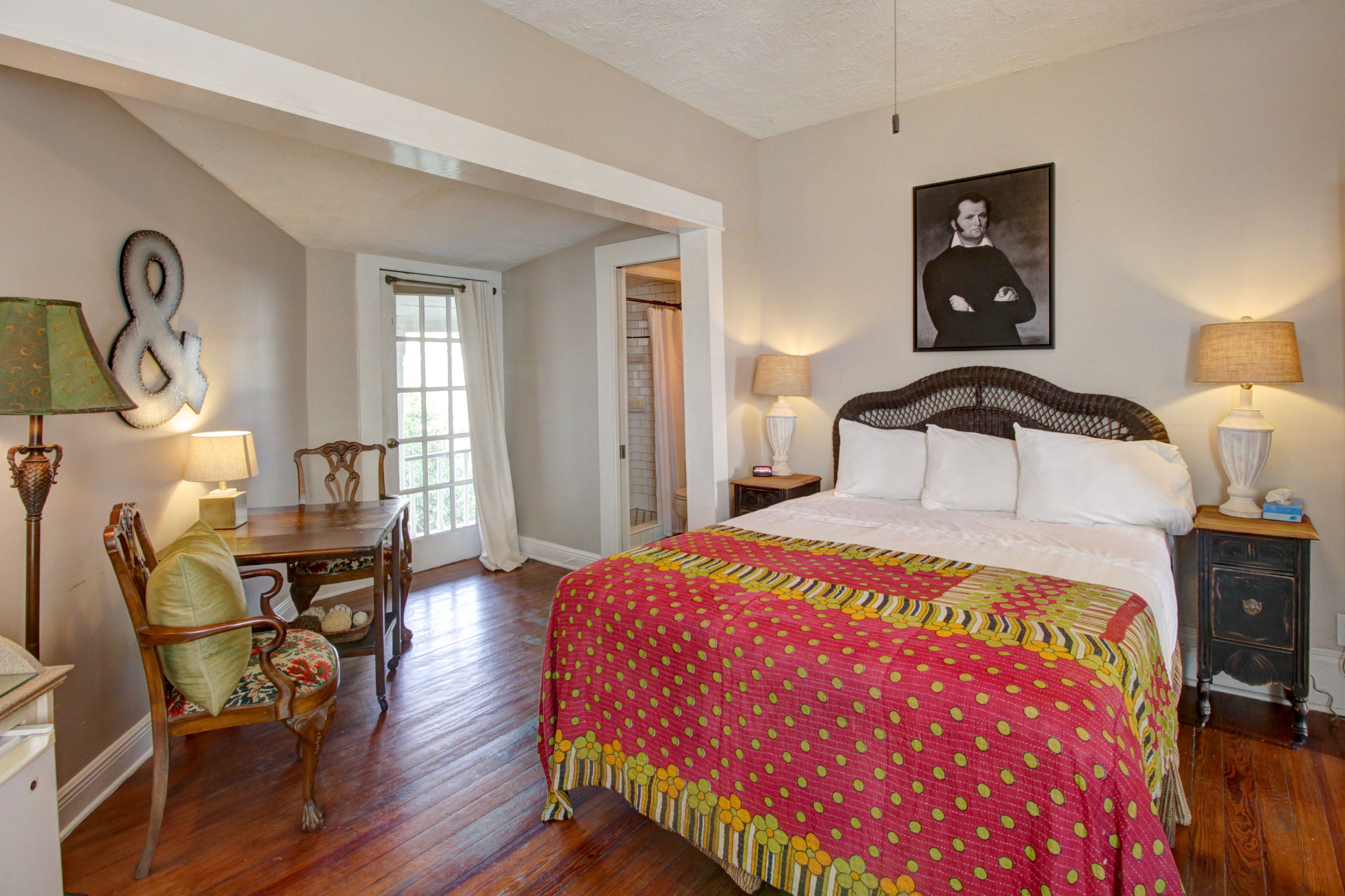 A bedroom with a large bed, a chair, a desk, and a nightstand.