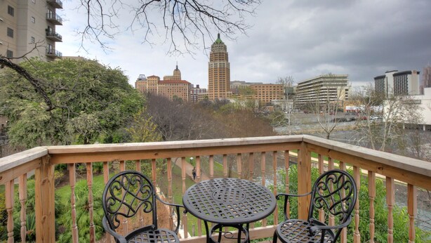 A wooden deck with a table and two chairs, overlooking a river and city buildings. - Inn on the Riverwalk (San Antonio)