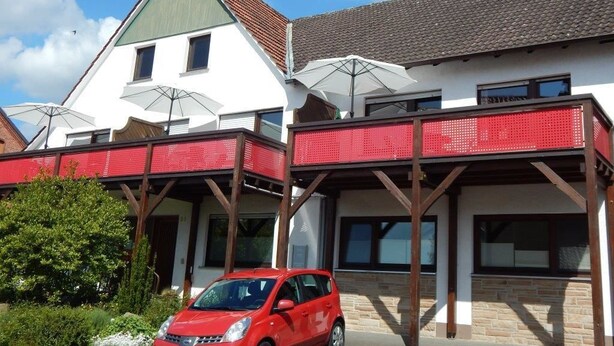 A two-story building with a red balcony and white walls. - Reiter- und Ferienhof Redder (Bad Driburg)
