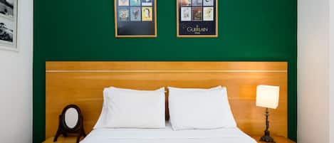 A neatly made bed with white linens, a wooden headboard, and a nightstand with a lamp.