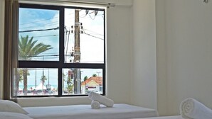 Una habitación de hotel con dos camas, un ventanal con vista a la playa y palmeras, y toallas enrolladas sobre las camas.