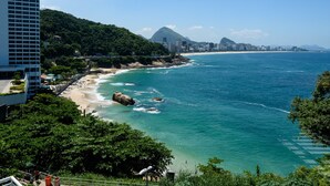 Paisagem costeira com praia, uma montanha imponente e um edifício moderno.