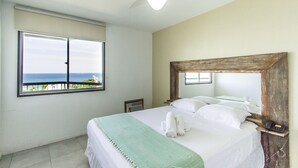 A bedroom with a large window, a ceiling fan, and a bed with white linens and a green throw blanket. - Omar do Rio - Apartamento V210 (Rio de Janeiro)