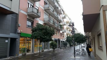 Una stretta strada cittadina fiancheggiata da edifici residenziali a più piani, con balconi e piccoli alberi.