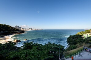 Un paisaje costero con vista al océano, una montaña y el horizonte de una ciudad a lo lejos.