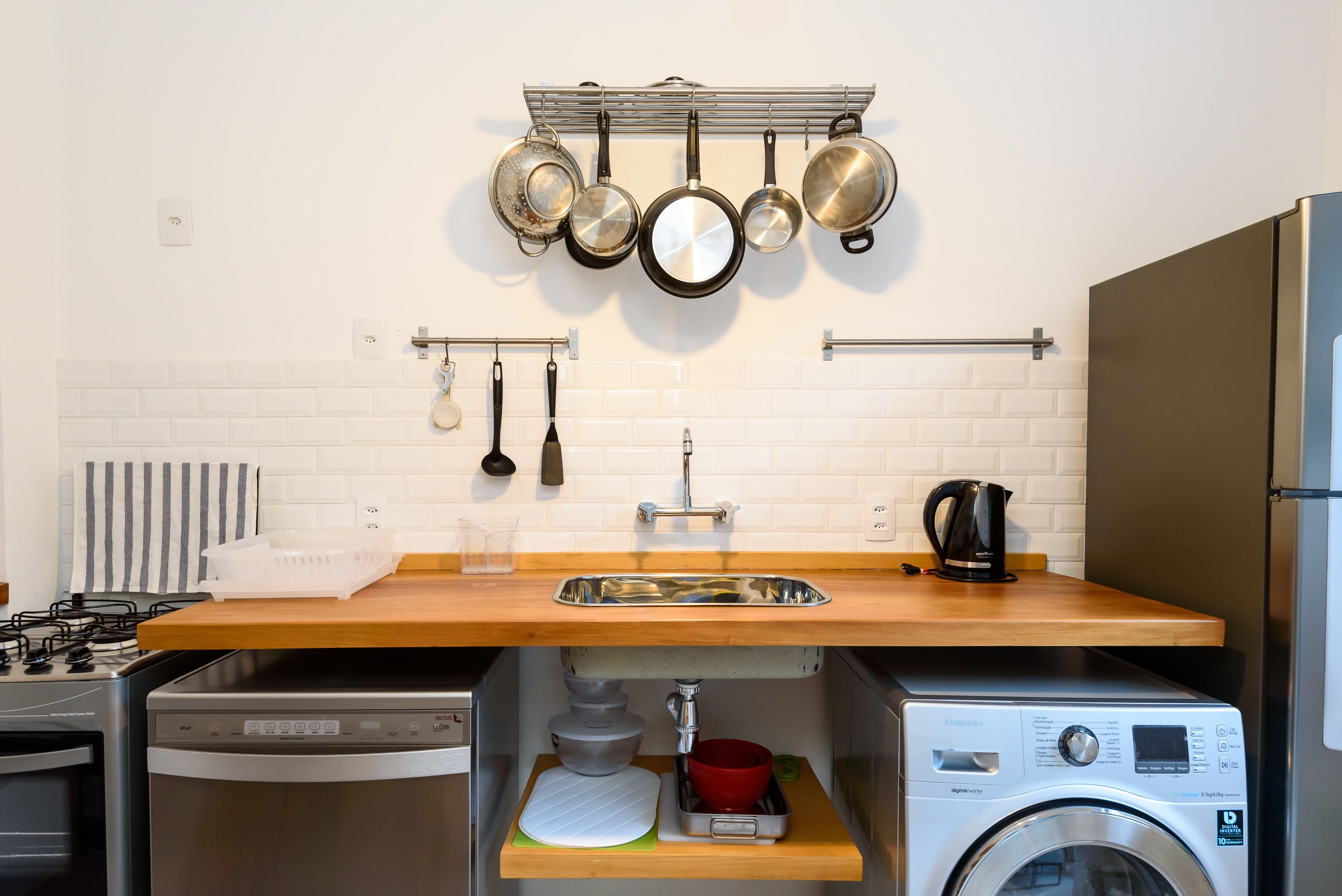 A compact kitchen with a wooden countertop, stainless steel appliances, and a hanging pot rack.