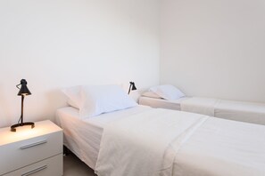 Un dormitorio con dos camas, cada una con ropa de cama blanca y mesitas de noche negras con lámparas.