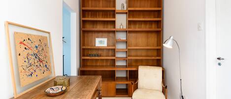 A room with a wooden bookshelf, a white chair, a wooden table, and a floor lamp.