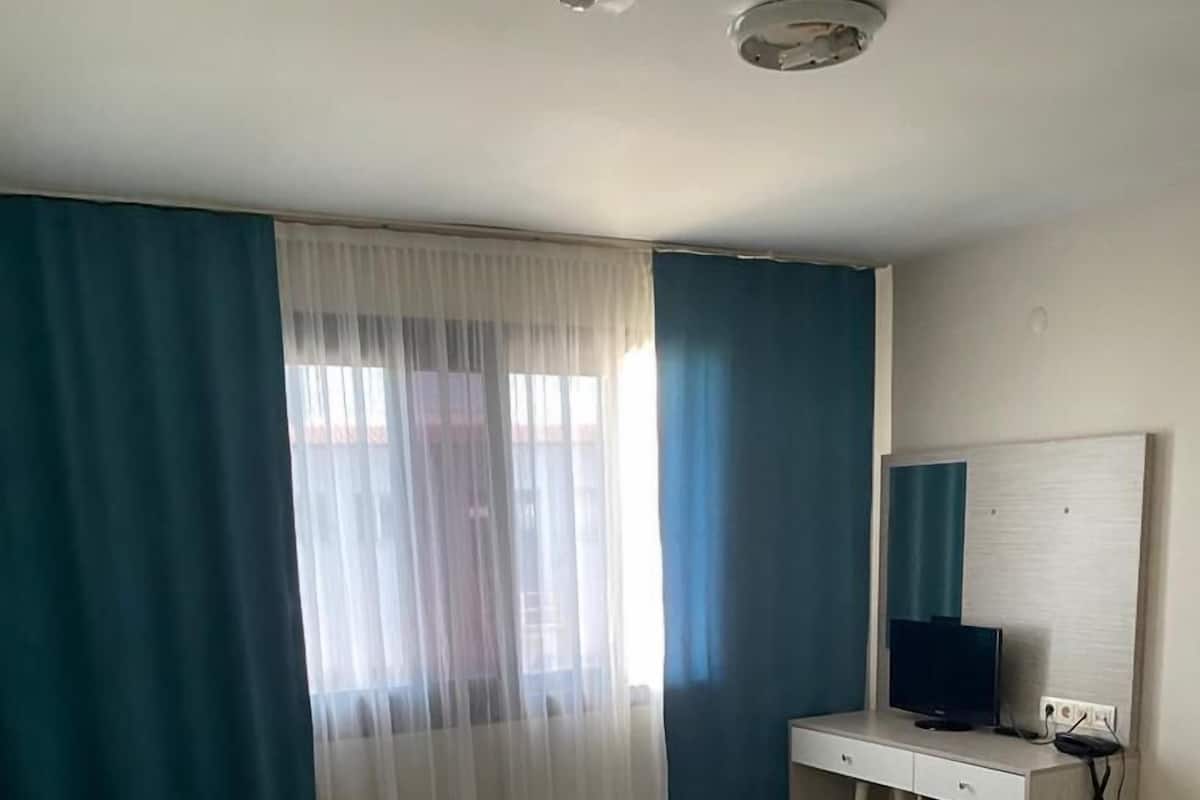 A hotel room with a bed, a desk, a television, and a window with curtains.