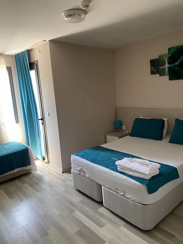 A hotel room with a bed, a bedside table, a nightstand, and a window with curtains. - Suya Hotel (Izmir)
