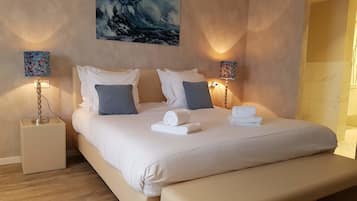 A neatly made bed with white linens, two pillows, and two rolled towels. There are two bedside lamps with floral designs on the nightstands.