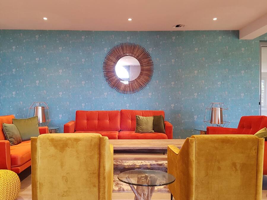 Una sala de estar moderna con una pared azul con textura, un espejo redondo grande y dos sofás rojos con cojines amarillos y verdes.