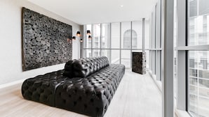 Un interior moderno con un sofá de cuero negro, una obra de arte en una pared de piedra y ventanas amplias que ofrecen vistas de la ciudad.