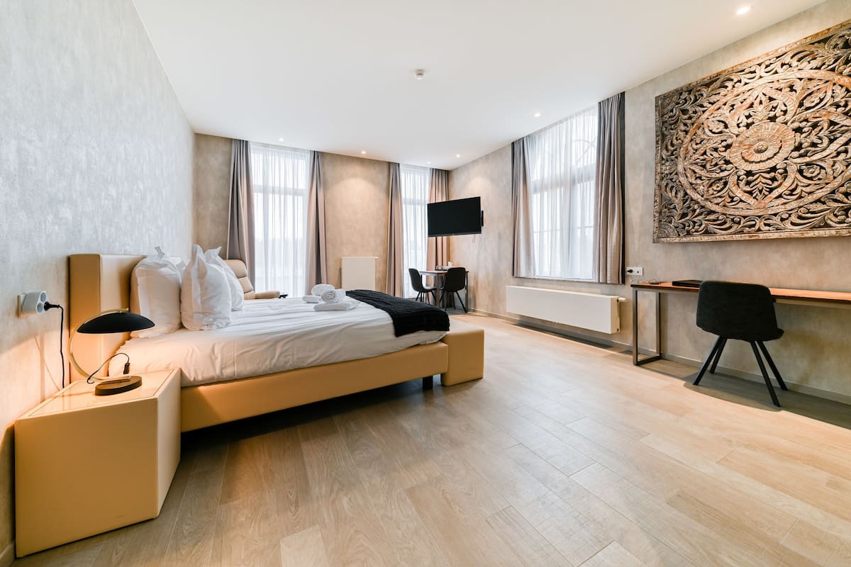 Quarto de hotel moderno com uma cama grande, uma escrivaninha, uma TV e um objeto decorativo na parede.