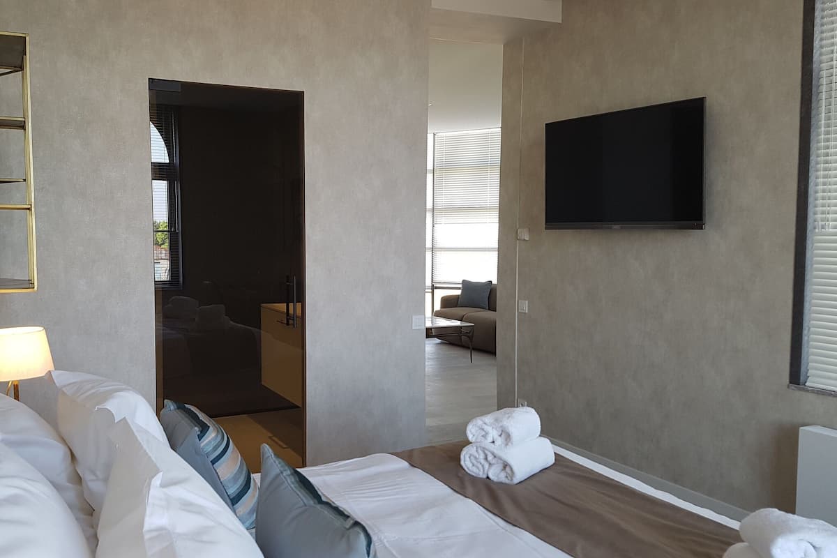 Quarto de hotel com cama, televisão, luminária, espelho e vista para a sala de estar.