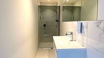 A modern bathroom with a glass-enclosed shower, a white vanity with a large mirror, and marble tiles.